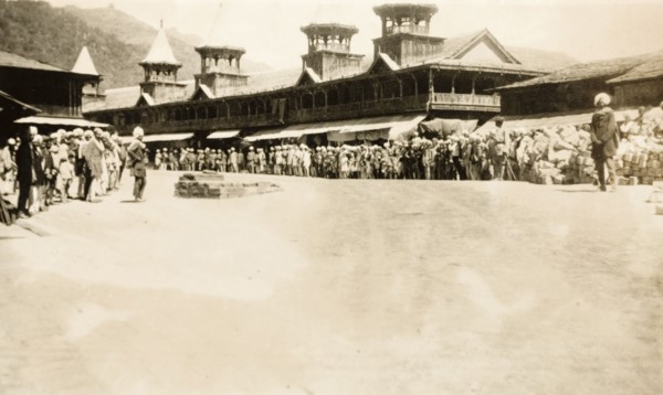 Crowds at a 'chowk' in Mandi, India. A crowd of people line up outside a row of shops with awnings