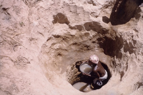 Waterhole near Tamale. A Ghanaian woman collects water in a pail from the bottom of a deeply-dug