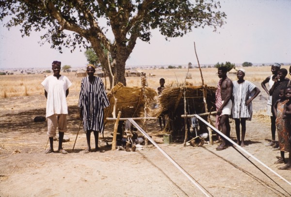 Boys weaving cloth at Pusiga, Ghana. Two young boys sit outdoors beneath thatched sun shelters as