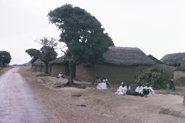 A Hausa village. Inhabitants of a Hausa village sit on the ground outside several square,