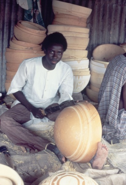 A Hausa potter decorates a bowl. A Hausa potter uses a metal tool to inscribe patterns onto a clay