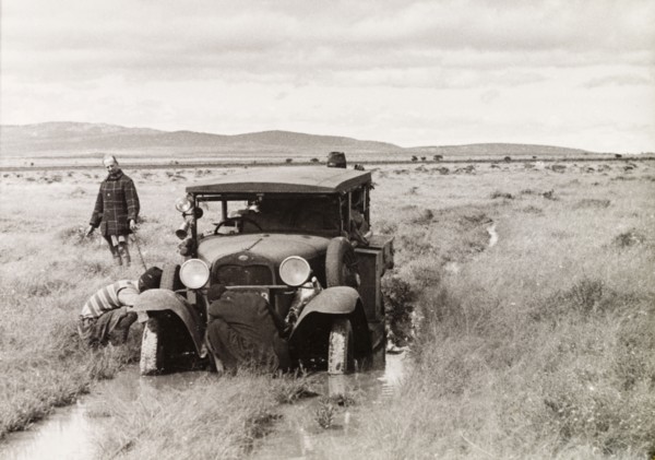Stuck in the mud. Several men attend to a car, which is stuck in the mud on a flooded country track