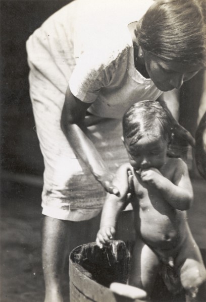 A European woman washes her child. A European woman bends over to wash her young child in a washtub