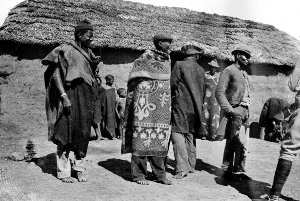 African men outside a hut. African men, possibly members of a Bantu-speaking tribe, mill about in