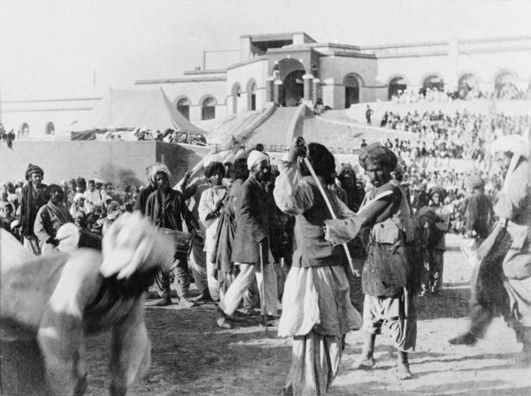 A display of swordsmanship. Musicians play as two swordsmen spar at an outdoor event. Sukkur, Sind,