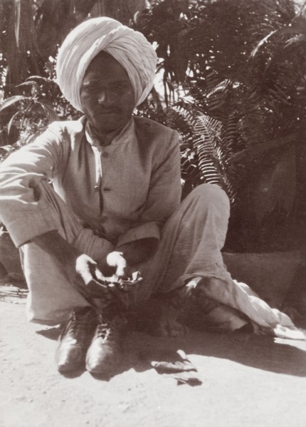 Indian man in Karachi. An Indian man squats on a street in Karachi, barefoot with his shoes