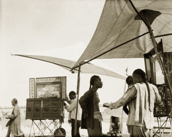 Peep boxes at a Chinese fair. Stallholders set up peep boxes beneath parasols at an outdoor fair.