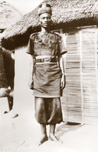 A Nigerian policeman at Minna. A uniformed Nigerian policeman stands outside a thatched village