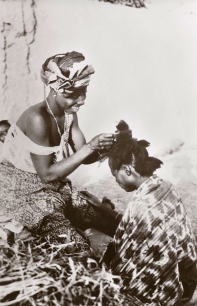 Hairdressing in Jos'. A Nigerian hairdresser smiles as she styles a customer's hair. Jos, Nigeria,