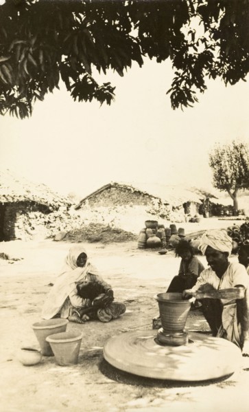 Indian craftsman at a potter's wheel. A craftsman sits beneath a shady tree as he sculpts a clay