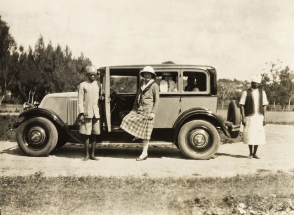 A head servant holds open a car door. An African head servant holds open the door of a car as a