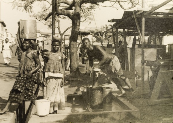 Collecting water from a hand pump, Accra. Men and women collect water from a hand pump on a street