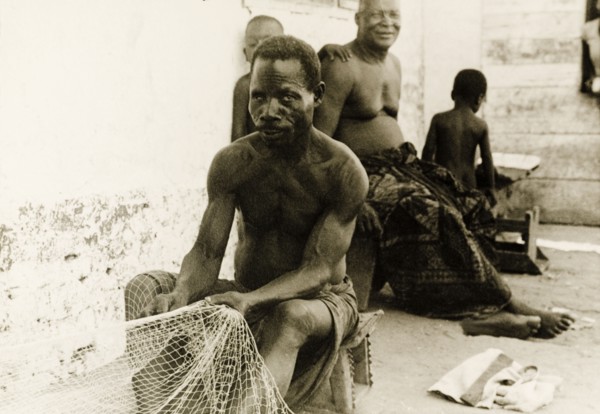 Fisherman repairing his nets, Ghana. A fisherman sits on a stool at the side of a street as he
