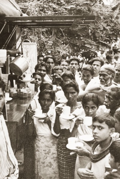 Drinking tea from a mobile kiosk. A group of people crowd around the hatch of a mobile kiosk, where