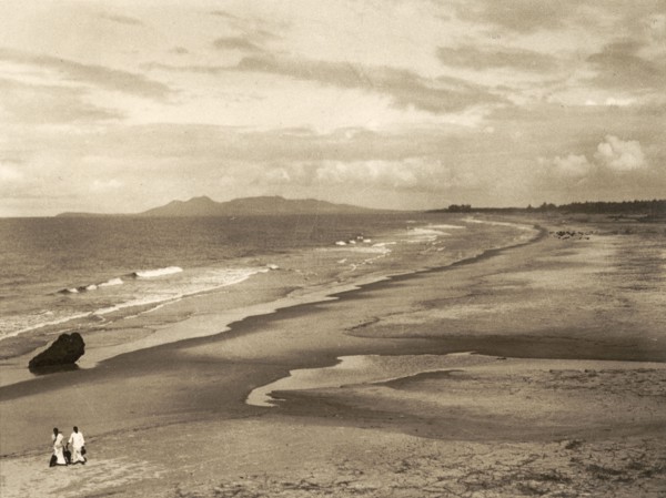 Malabar Coast and Mount Deli. Two tiny figures walk along a vast sandy beach on the Malabar Coast