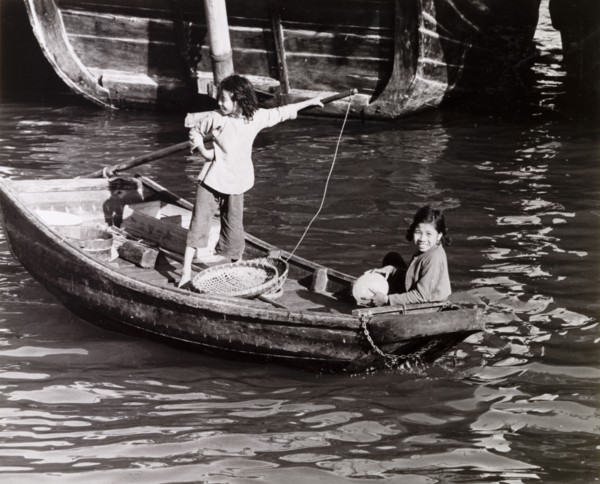 Chinese girls steer a sampan. Two girls travel aboard a scull-propelled sampan in Aberdeen Harbour,