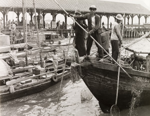 Fishing in a Hong Kong harbour. Fishermen stand at the bow of their sampan, dipping long-handled