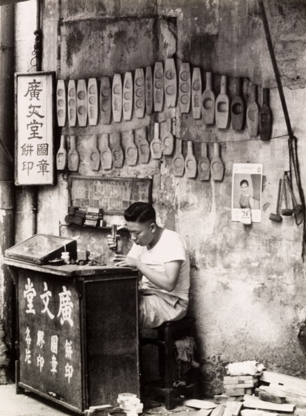A mould maker, Hong Kong. A Chinese mould maker sits at his street stall, carving seals and cake