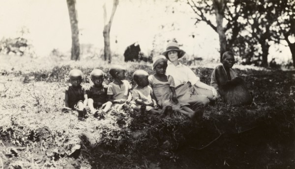 European woman with Chaga children. A European woman sits on a grassy bank with a Chaga woman and