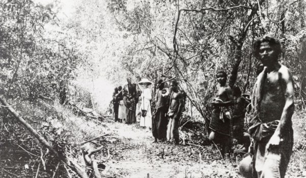 Beaters on an elephant drive, Ceylon. A European woman stands in a jungle clearing with a team of