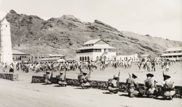 Policing the Aden riots, 1947. Armed police or soldiers form a defensive barrier behind a low wall,