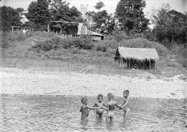 Children playing in water, Burma. Four young Burmese children stand in a circle holding hands as