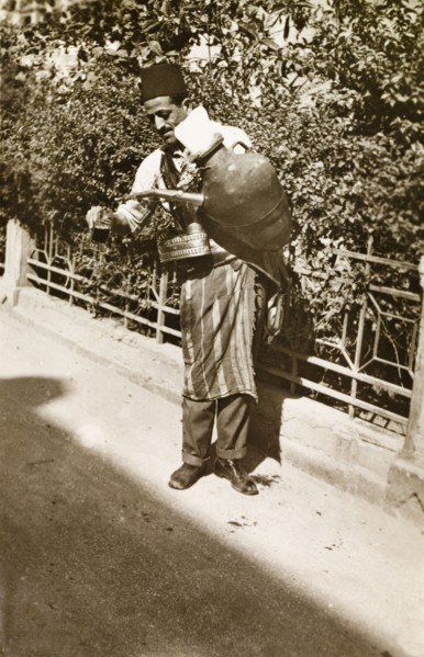 Lemonade seller, Palestine. A lemonade seller pours out a drink from a large jug strapped to his