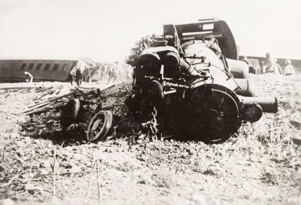 Derailed steam locomotive at Ras el Ain. A steam locomotive lies in pieces on a railway embankment,