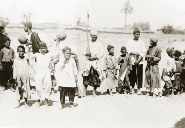Palestinian villagers at harvest time. Men and boys stand in line with agricultural tools and