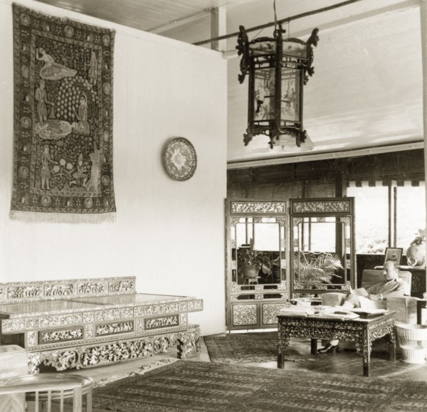 Asian artefacts in a colonial drawing room, British Malaya. Dr Reid Tweedie sits reading in the