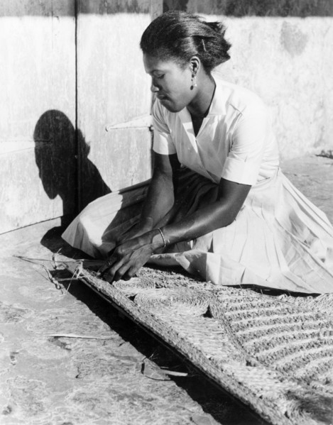 Weaving a palm mat, Dominica. A young woman sits on the ground as she weaves a mat from palm fibre.