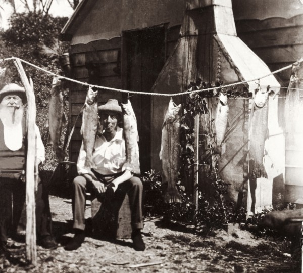 Admiring the day's fishing catch, New Zealand. Two men smoking pipes sit and admire a selection of