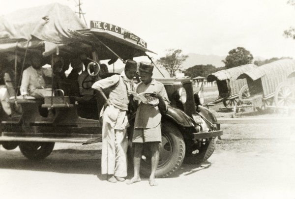 A 'CPS Motor Service' bus. The drivers of a 'CPS Motor Service' bus stand and read a magazine