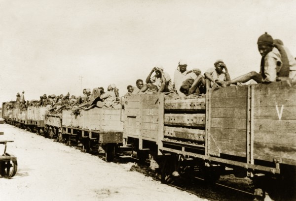 African schutztruppes travel by rail. African schutztruppes travel in crowded, open railway wagons