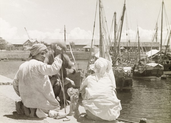 The Old Harbour at Stone Town. Three men sit beside the Old Harbour at Stone Town, with several