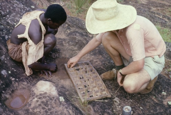 Playing omweso at Kojja. A British man identified as Martin Beadle squats down to play omweso