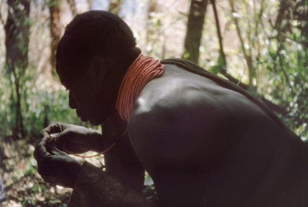 Rescuing a broken necklace. A Karamojong porter working with a British forestry survey team rescues