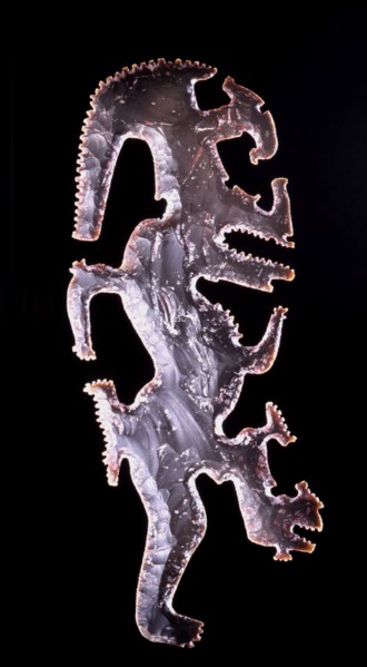 Eccentric axe with representation of the God K, the god of lightning, recognised by the torch running through his forehead and an elongageted serpentine leg