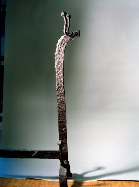 Detail of the upper end of a wrought iron fire dog in the shape of a stylized bovine animal with balled horns