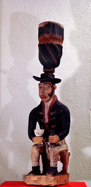Drum with support carved as the figure of a seated European trader with gin bottle and glass