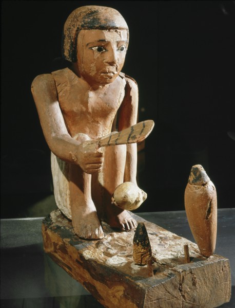 A male cook fans the fire in preparation for roasting the duck he holds in his left hand