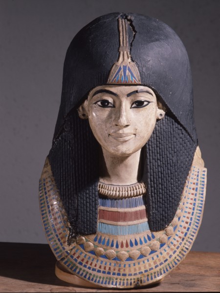 A mummy mask of a man wearing an elaborate collar and a heavy wig adorned with a lotus blossom