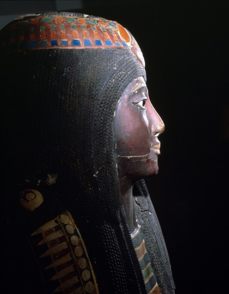 Upper part of an anthropomorphic coffin with blackened face, lotus ornamented wig, chest ornaments, and a picture of the deceased kneeling to offer flowers to Osiris