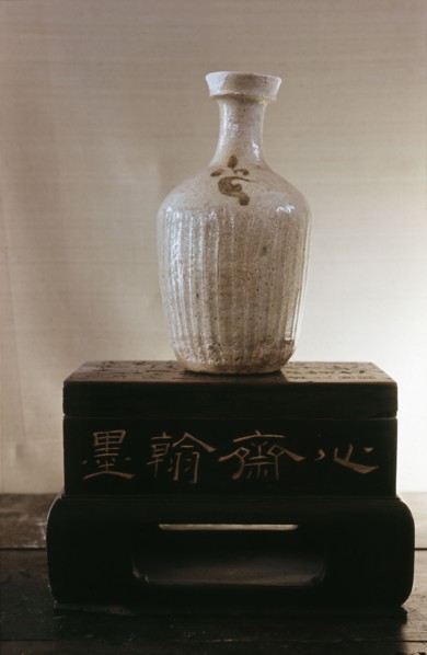 A vase with a white glaze, serrated body and small flower motif painted in black