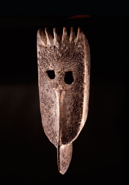 A wooden face mask with remnants of red seeds attached