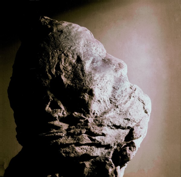 Cast of a man's head with his mouth partly covered with lava