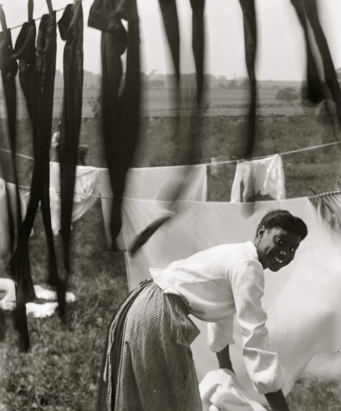 Black and white, an informal portrait of a young Black woman surrounded by laundry in Newport, R.I. 1902