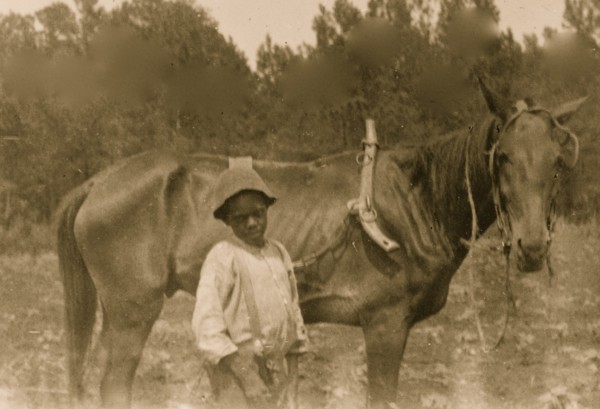 African American boy standing with horse attached to plow 1899
