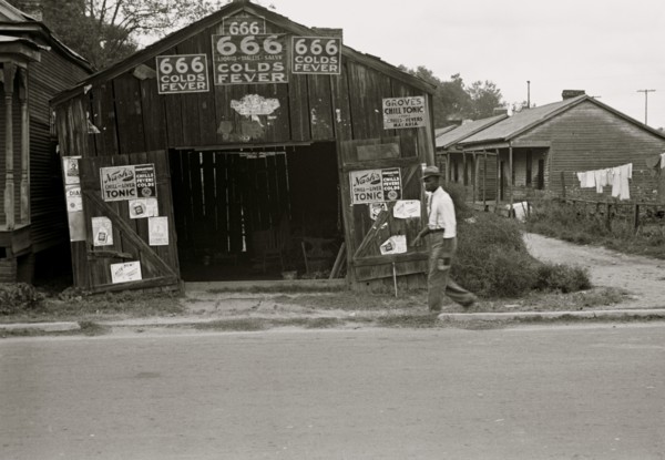 African American walks in front of, Advertisements for popular malaria cure, Natchez, Mississippi 1935
