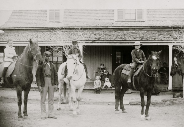 Afro-American enlisted man standing by three officers' children on horseback, Fort Verde, Arizona 1886